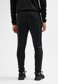Black athletic pants made of smooth, stretchy fabric, featuring a tapered design and elastic waistband with a subtle sheen.