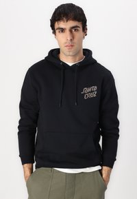 Črna kapuca pulover s kanalsko žepom, ki na prsih vsebuje teksturirano logotip "JANTA CRUZ" v kontrastnih barvah.