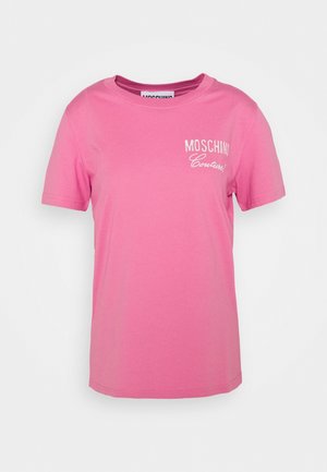 Vaaleanpunainen, lyhythihainen T-paita, jossa on pyöreä pääntie ja valkoinen "MOSCHINO Couture!" -teksti vasemmassa rinnassa.