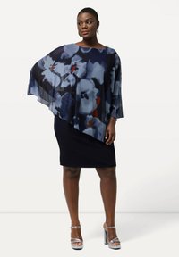 Top de capa semitransparente con estampado floral en tonos navy sobre un vestido negro ajustado. Presenta un diseño fluido y tacones plateados con correa al tobillo.