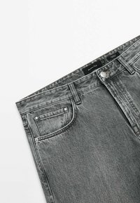 Jean en denim gris taille haute avec poche avant, passants de ceinture, bouton en métal et étiquette de marque visible à la taille.