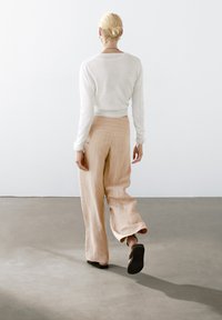 Witte lange mouwen trui gecombineerd met lichtbeige wijde broek met subtiele verticale strepen. Model draagt donkere, platte sandalen.