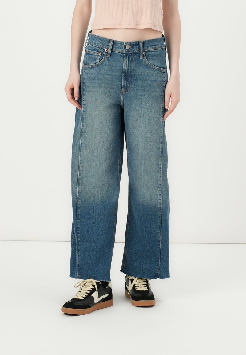 Light blue wide-leg jeans made of denim, featuring a high waist, contrast stitching, and a gradual fade at the cuffs. Worn with black sneakers.