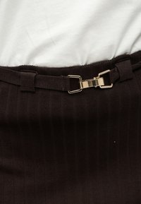 Καφέ υφασμάτινο με ρίγες, λεπτή ταινία και λεπτομέρεια με αγκράφα σε χρυσή απόχρωση στη μέση, συνδυασμένο με λευκό τοπ που φαίνεται μερικώς από πάνω.