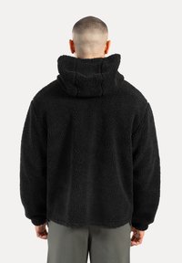 Czarna polarowa kurtka z kapturem, charakteryzująca się teksturowaną, puszystą powierzchnią oraz luźnym krojem, zaprojektowana z myślą o komforcie i ciepłe.