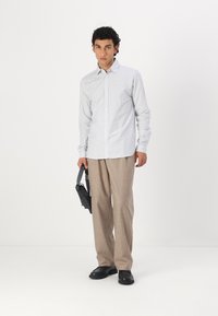 Cămașă cu dungi în albastru deschis și alb, asociată cu pantaloni bej. Modelul ține o geantă neagră și poartă pantofi negri. Design simplu.
