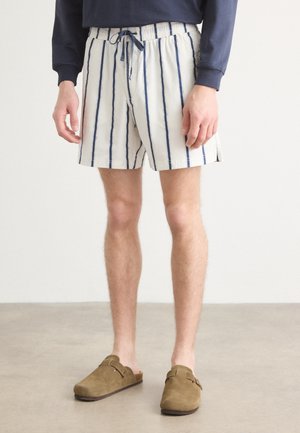 Striped swim shorts in white and navy, made of lightweight fabric, featuring an elastic waistband with a drawstring and side slits.