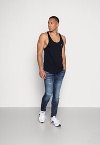 Sort med svart tanktop sammen med blå slitte jeans og hvite joggesko. Antrekket har en tettsittende design og en subtil logo på toppen.
