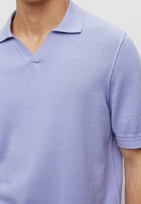 Man wearing a light purple short-sleeve knit polo shirt with a V-neck collar, shown from neck to mid-torso.