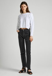 Maglione corto a trecce bianco abbinato a jeans grigi scuri a vita alta e sandali neri con tacco largo. Design semplice e pulito.