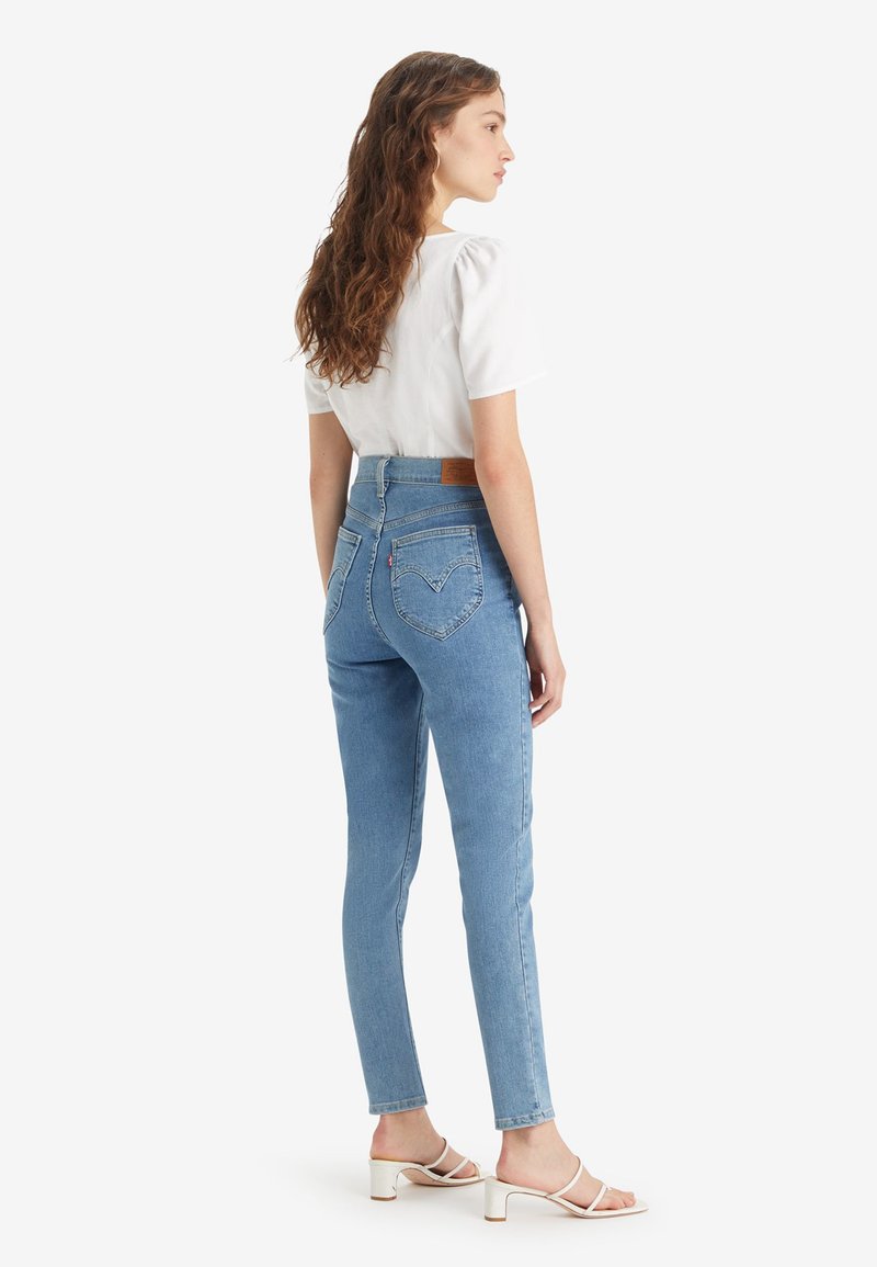 Jean bleu taille haute en denim, au design ajusté, style cinq poches, avec un motif de couture distinct sur la poche arrière.