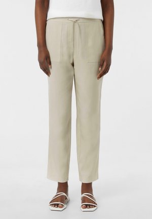 Lichtbeige broek met een trekkoord in de taille, twee voorkanten zakken, een rechte pijp ontwerp en een gladde textuur. Gecombineerd met witte sandaaltjes met bandjes.