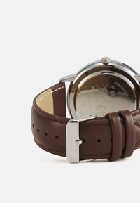 Bracelet de montre en cuir marron avec boucle en métal argenté, doté d'un boîtier en acier inoxydable poli et d'un design de fond rond.