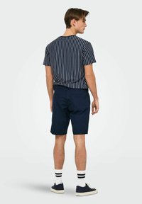 Shorts bleu marine à motif uni, associés à un t-shirt rayé bleu marine et blanc. Le modèle montre une coupe décontractée de dos.