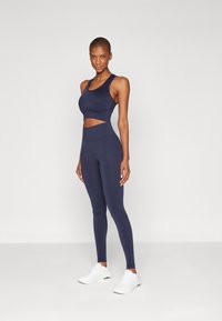 Navy atletisk crop top med utskjæringsdetalj og matchende høyt midje leggings, laget av glatt og elastisk stoff. Kombinert med hvite joggesko.