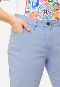 Jeans de denim azul claro con un corte ajustado, un bolsillo frontal y un botón de metal negro en la cinturilla, con detalles de costura sutiles.
