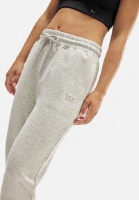 Pantalones de chándal grises claros confeccionados en una tela suave con cinturilla elástica y cordón. Presenta un logo bordado en el muslo.