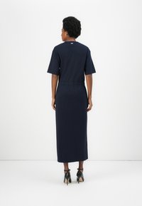 Μπλε ναυτικού, μακρύ φόρεμα με κοντό μανίκι και εφαρμοστό μέσο, με άνοιγμα στην πλάτη και λείο ύφασμα. Συνδυασμένο με μαύρες ψηλές γόβες.