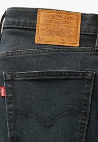 Tmavě modré džíny z denimu s koženou nášivkou značky "LEVI STRAUSS & CO." a červeným štítkem na kapse. Mají dvojité švy a klasický střih.