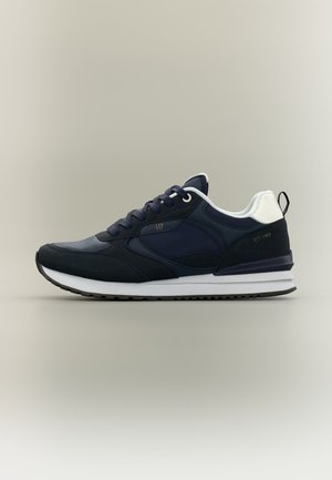 Baskets de sport bleu marine et noires avec semelle blanche, accent talon blanc et languette de tirage noire, brodées sur le côté avec "EST. 1969" et "GAP".