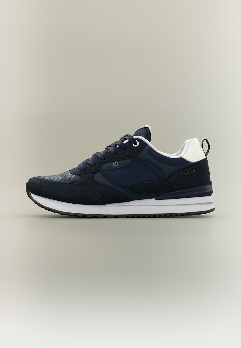 Baskets de sport bleu marine et noires avec semelle blanche, accent talon blanc et languette de tirage noire, brodées sur le côté avec "EST. 1969" et "GAP".