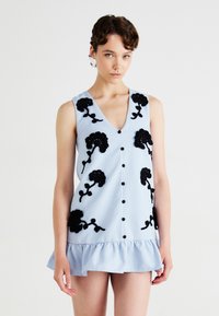 Light blue sleeveless dress with a v-neck, featuring black floral embroidery and buttons down the front; ruffled hem at the bottom.