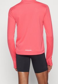 Langærmet sports top i lys koral, lavet af glat stof. Har en høj krave og et reflekterende hvidt detaljer ved kanten.