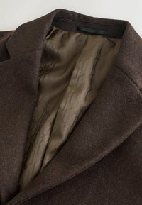 Brauner Mantel aus strukturiertem Wollstoff mit einem Reverskragen, der ein geschmeidiges olivgrünes Futter mit einem dezenten geometrischen Muster zeigt.