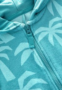 Turkis zip-up hættejakke lavet af et blødt, tekstureret stof. Designet inkluderer et palmebladsmønster og en matchende lynlås.