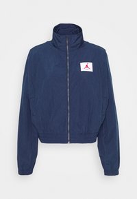 Navy blue krótka kurtka z wysokim kołnierzem, zamek błyskawiczny z przodu, elastyczny pas i biały haft z czerwonym logo.