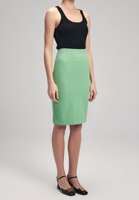 Svart ribbad linne kombinerat med en knälång, mintfärgad penningkjol och svarta klackar med guld detaljer. Slät textur, figurnära design.