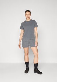 T-shirt en coton gris à manches courtes, associé à un short rayé gris. Porté avec des chaussures de sport noires et des chaussettes noires jusqu'aux genoux.