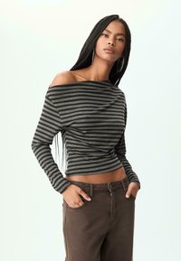 Gestreepte off-shoulder top in donkergrijs en zwarte stof met een aansluitende taille en lange mouwen, gecombineerd met hoge, bruin gekleurde broeken.