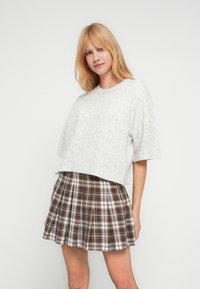 Γκρι κοντομάνικο πουλόβερ cropped, σε συνδυασμό με καφέ και λευκή καρό πλισέ φούστα με απαλή υφή υφάσματος.