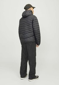 Sort pufferjakke med et chevron quiltet design, hætte, parret med sorte cargo bukser og sneakers. Bagview, ensfarvet baggrund.