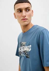 Blaues Baumwoll-T-Shirt mit einem Grafikdruck von Palmenblättern und weißem Text. Klassische Passform, kurze Ärmel und runder Halsausschnitt.