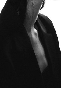 Blazer noir à col ouvert, dévoilant un cou lisse. Tissu doux avec une texture subtile, mettant en valeur un design épuré et minimaliste.