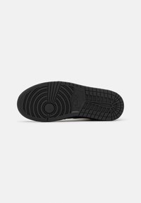 Semelle de chaussure Nike noire avec motifs de bande de roulement circulaires et rectangulaires et logo Nike au centre sur un fond clair.