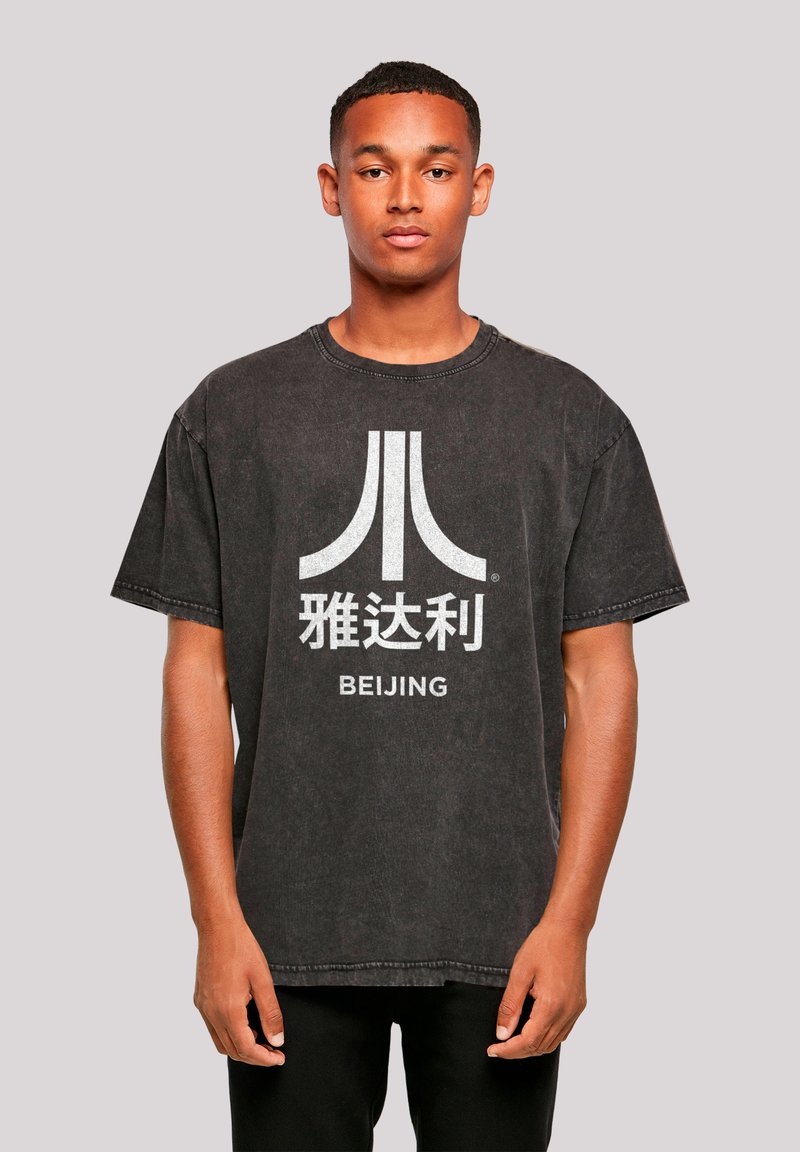 Black oversized t-shirt made of cotton, featuring a large white graphic design with text and symbol, ribbed crew neck, and short sleeves.