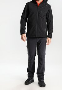 Veste noire résistante aux intempéries avec zip, capuche et poches latérales. Assortie à un pantalon noir à zip amovible et à des chaussures noires robustes pour une utilisation en extérieur.