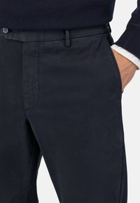 Pantalones de mezcla de algodón en color navy con textura suave, que cuentan con un delantero plano, bolsillos laterales y cierre de botón. Ajuste hecho a medida con pasadores para cinturón.