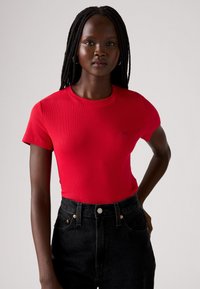 Czerwona prążkowana koszulka z okrągłym dekoltem i krótkimi rękawami, zestawiona z czarnymi, wysokim stanem jeansami zapinanymi na guziki.