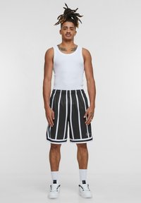 Svarta sportiga shorts med vita vertikala ränder, parat med en figurnära vit linne. Modellen bär vita strumpor och sneakers.