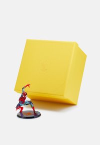 Samlarfigur av en Spider-Man-karaktär i genomskinlig röd och blå, placerad bredvid en solid gul låda med en texturerad yta.