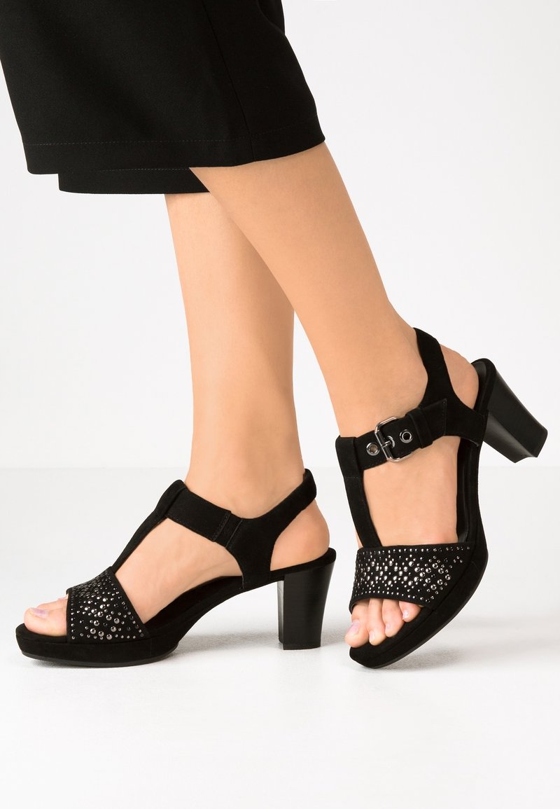 Sandales à talons en daim noir avec bout ouvert, bride de cheville ajustable et panneau avant orné de strass avec des accents métalliques.