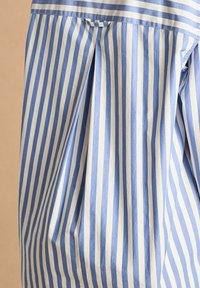 Blue and white striped cotton fabric with vertical lines. Features pleats and a folded hem, showcasing a smooth, textured surface.