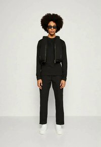 Conjunto desportivo preto com uma jaqueta com fecho éclair e design cropped, emparelhada com calças de perna reta e ténis brancos.