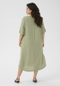 Vestido verde oliva, de longitud hasta la rodilla, con mangas cortas, corte relajado y cuello redondo. Tela suave con un ligero brillo.