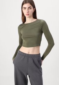 Olive green long-sleeve cropped top made from a smooth fabric, paired with gray sweatpants featuring an elastic waistband and side pockets.