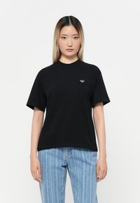 Black cotton t-shirt with short sleeves and a crew neckline, featuring a small heart-shaped logo on the left chest. Classic fit.